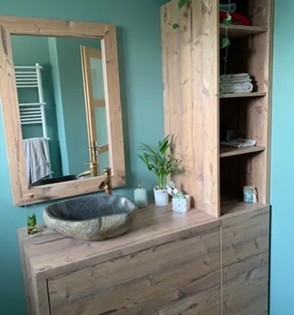 Meuble de salle de bain en bois brut avec miroir et plante.